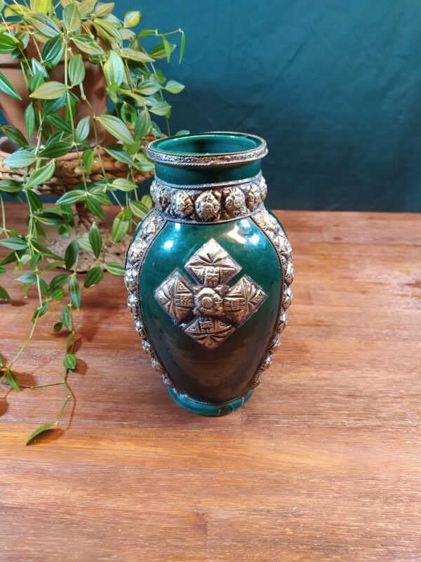 Vase oriental en céramique vintage avec ornements en métal sur fond bleu/vert.